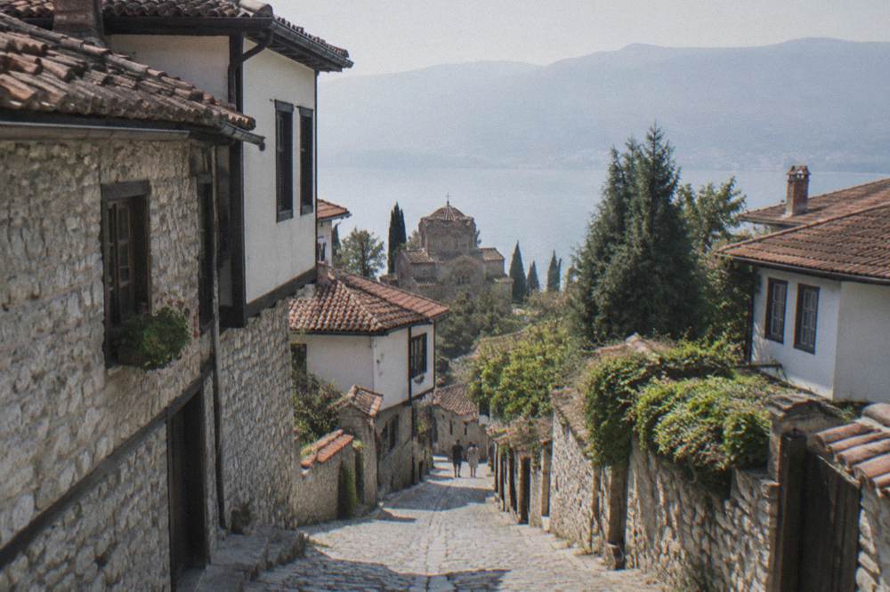 A narrow cobbled street in Ohrid lined with stone houses and a church tower beyond