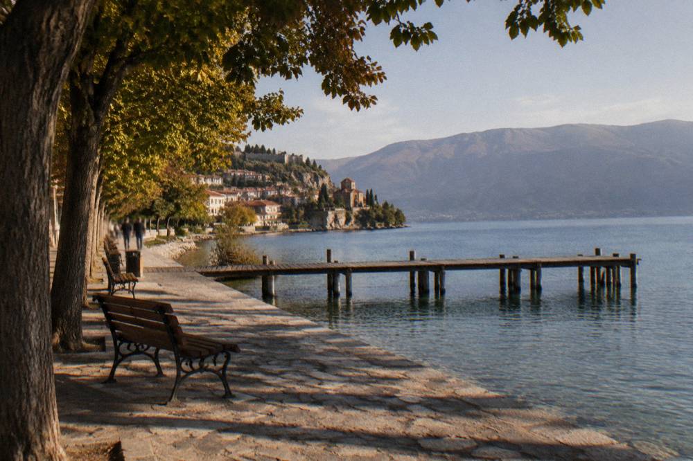 A wooden pier extending into clear turquoise water with wooded hills behind