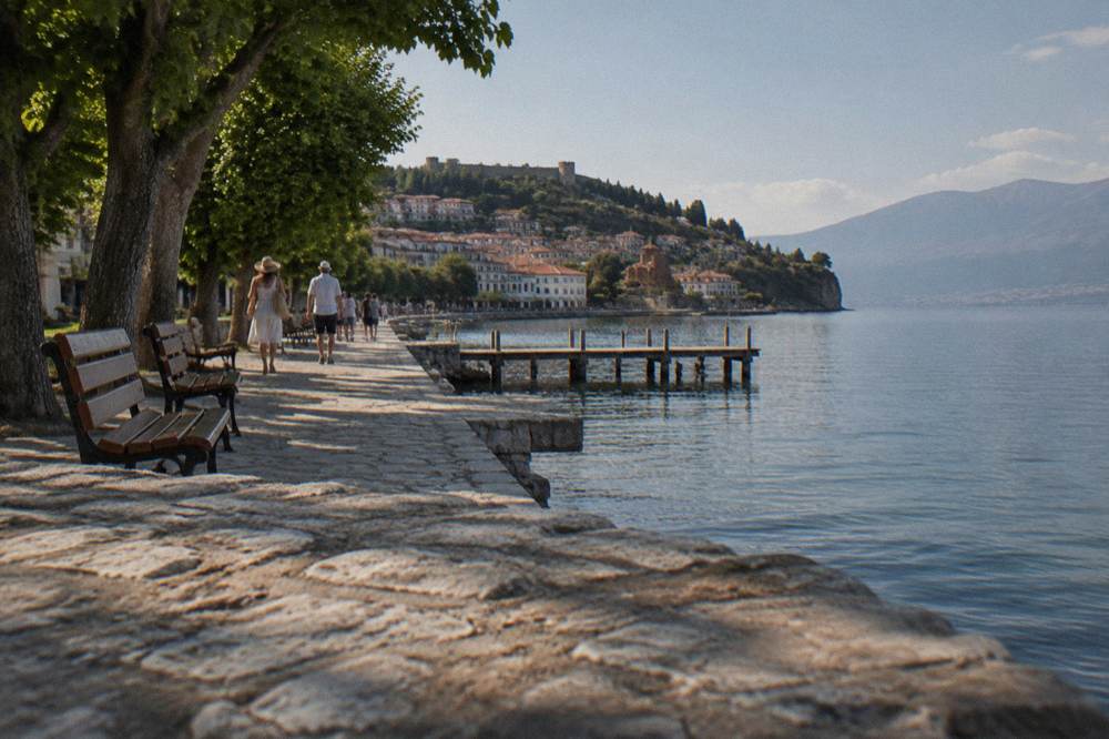 People strolling along a lakeside promenade with stone buildings at golden hour