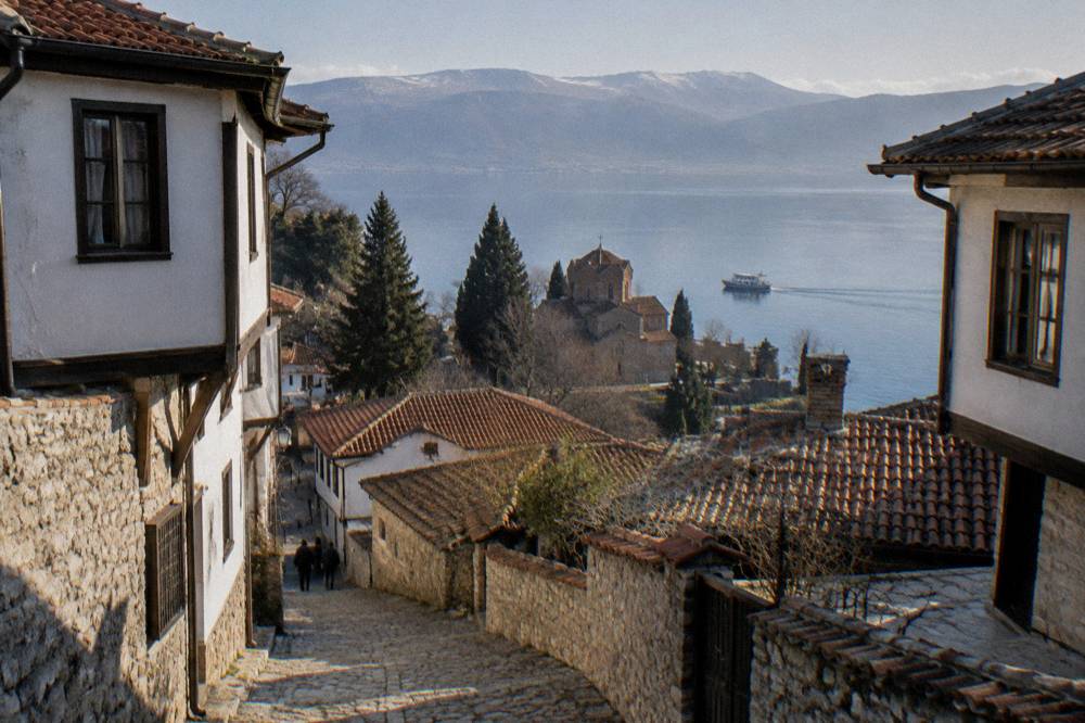 A small boat cruising along Lake Ohrid past a stone church on the shoreline
