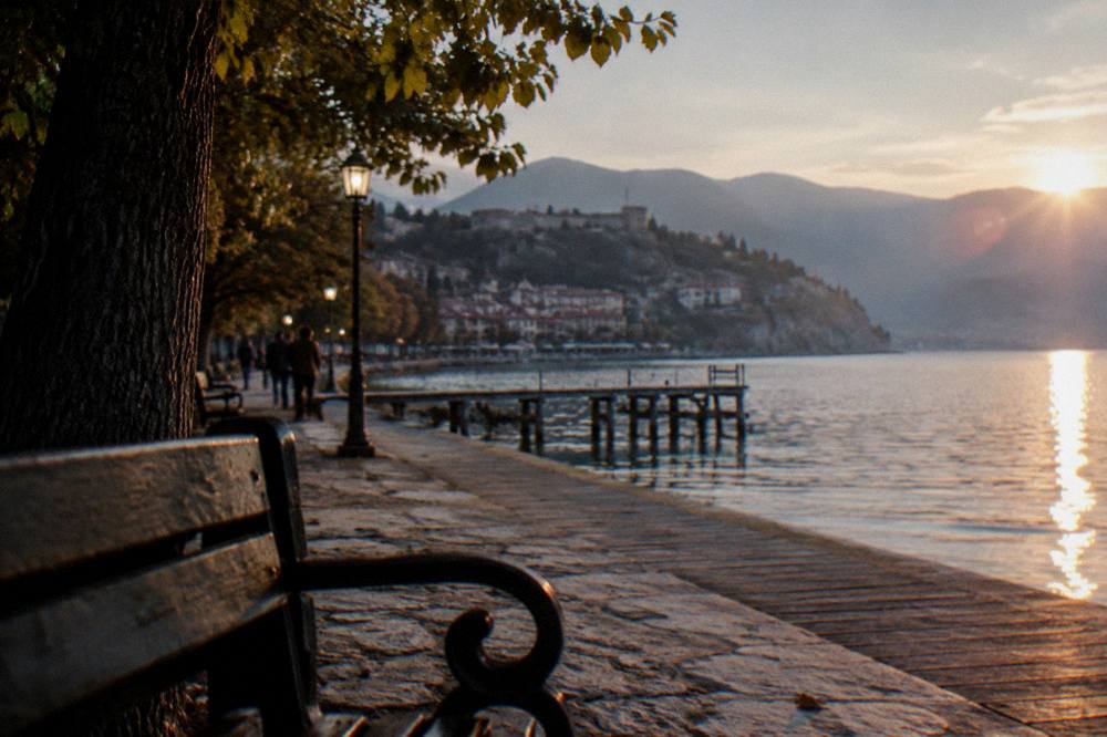 An evening arrival at a lakeside promenade with lamps reflecting on the water