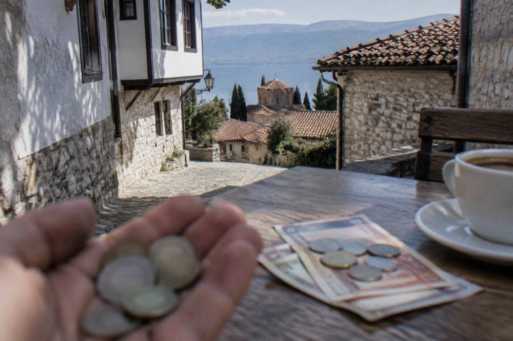 Macedonian denar banknotes and coins on a wooden café table beside a coffee cup