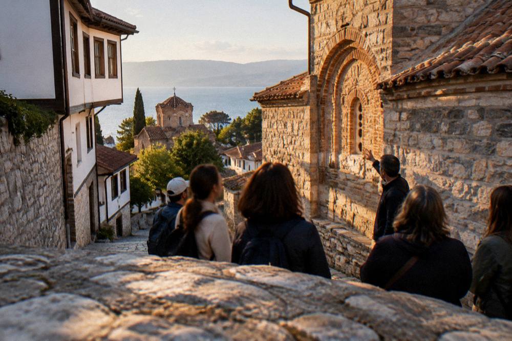 A guide pointing out details on a stone church facade to a small group of visitors in Ohrid