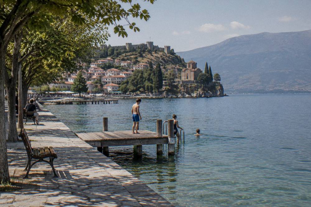 Swimmers entering clear green water from a wooden jetty on Lake Ohrid