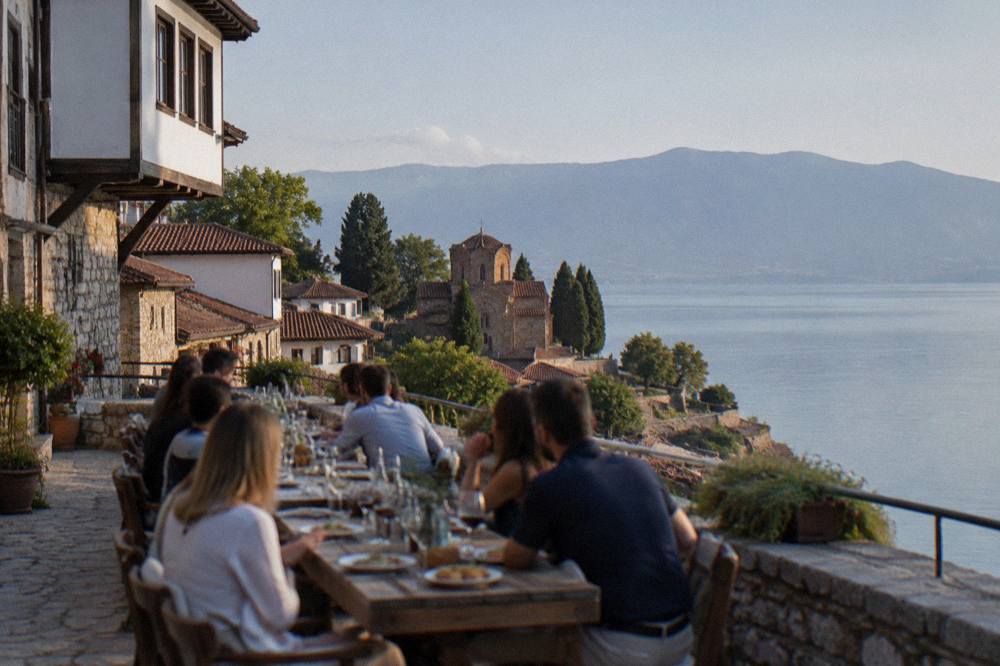 A long table of diners eating and drinking on a terrace above Lake Ohrid at dusk