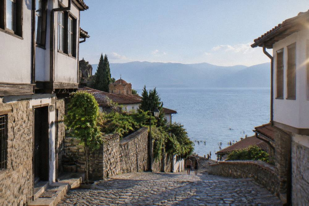 People swimming from a pebble beach into clear turquoise water on Lake Ohrid