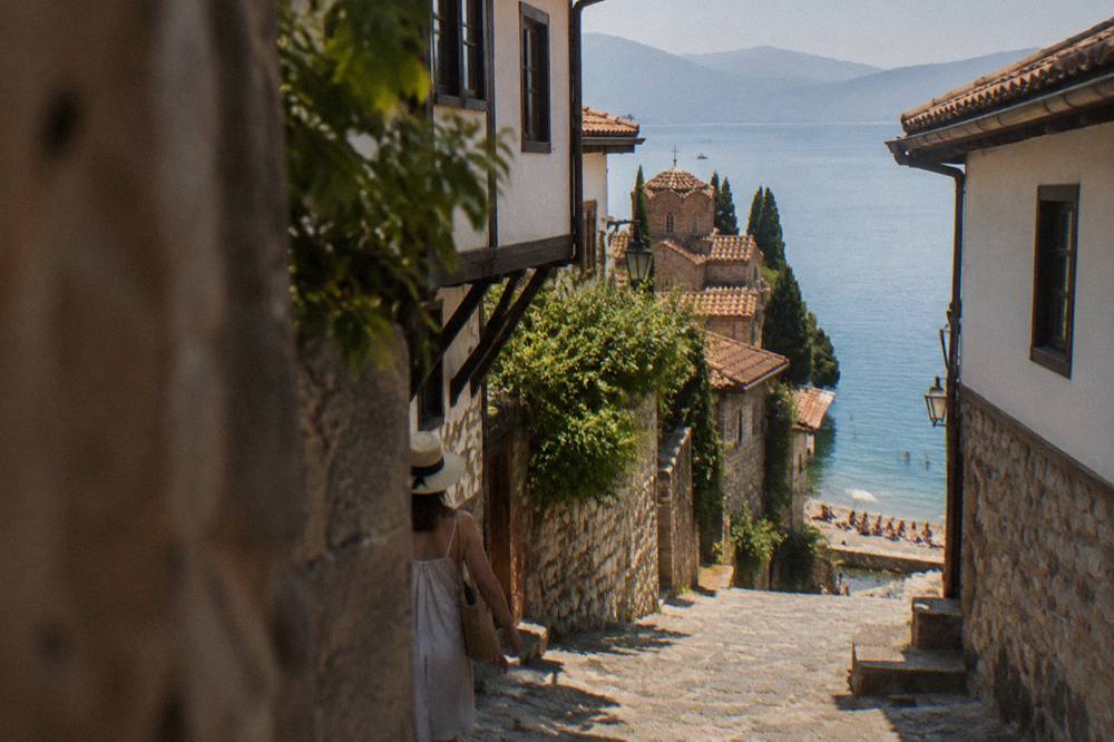 Swimmers and sunbathers on a pebble beach beside calm turquoise water at Lake Ohrid in summer