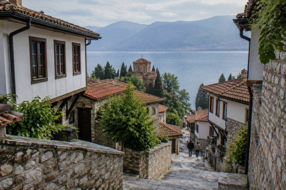 Stone steps climbing between old houses toward a fortress wall above a lake