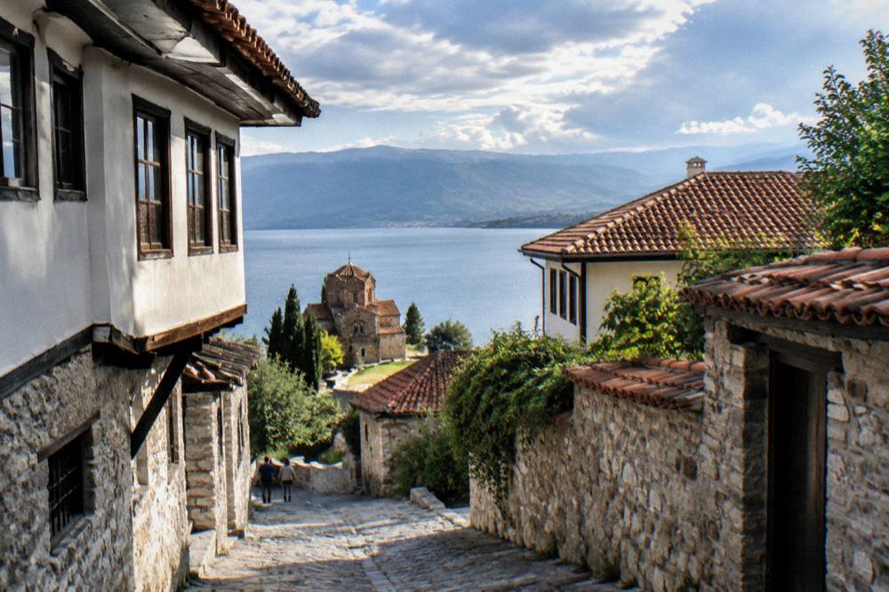 A small wooden monastery church on a grassy point above a turquoise lake