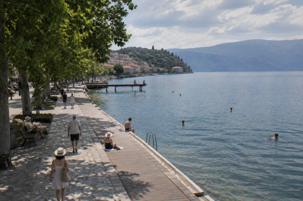 Swimmers and spectators along a lake promenade on a bright summer morning