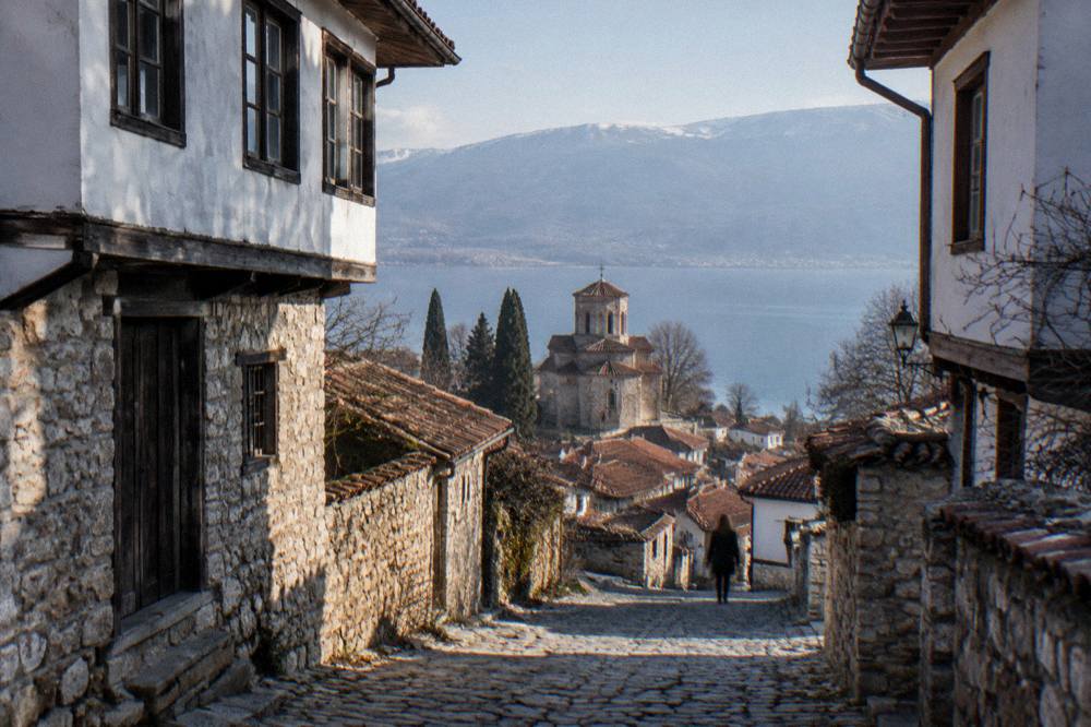 A stone church tower above red rooftops leading down to a wide blue lake