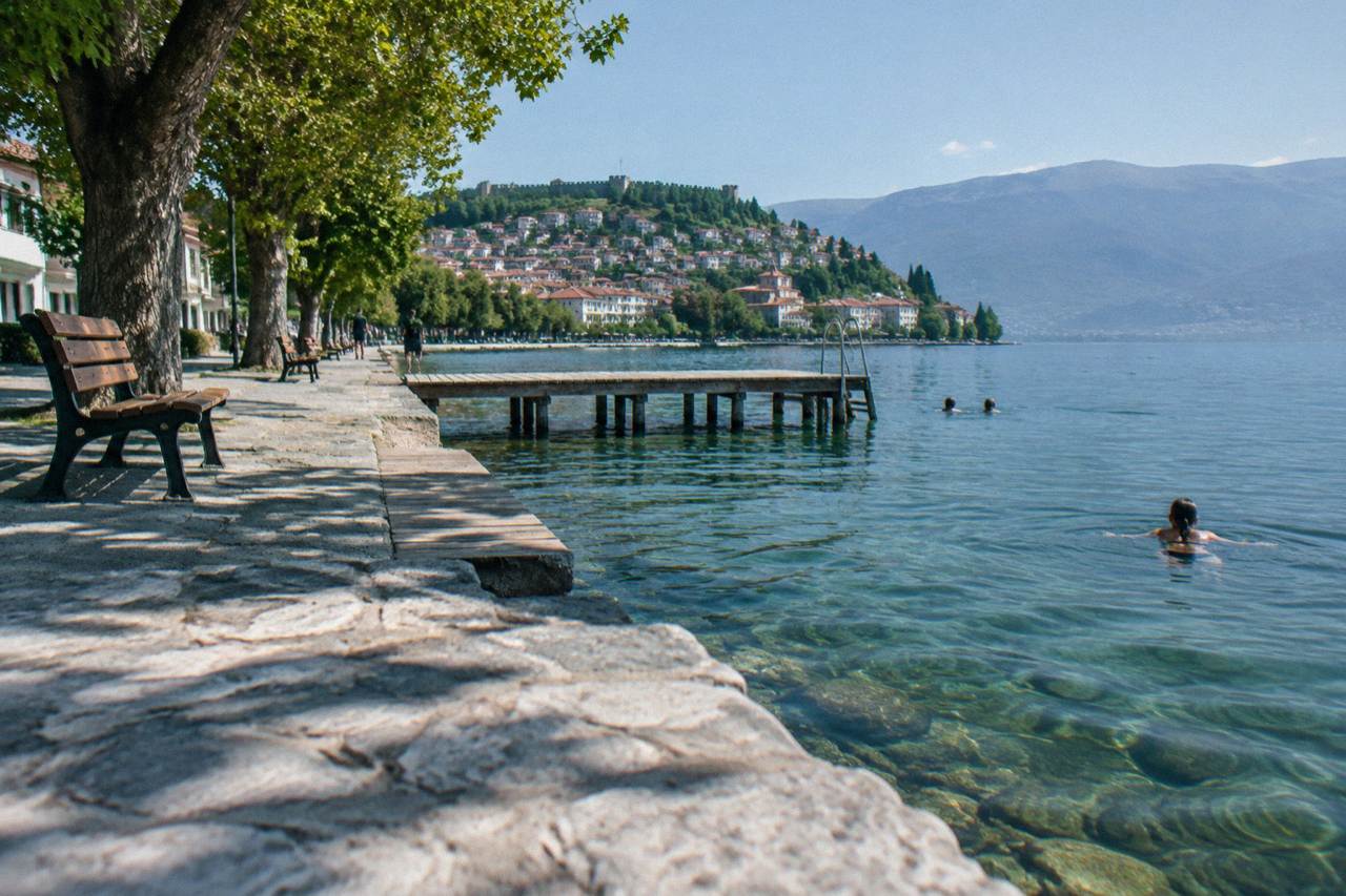 Swimmers in clear green water beside a wooden jetty on the shore of Lake Ohrid