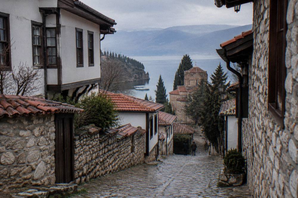 A boat on turquoise water near a wooded shoreline at the southern end of Lake Ohrid