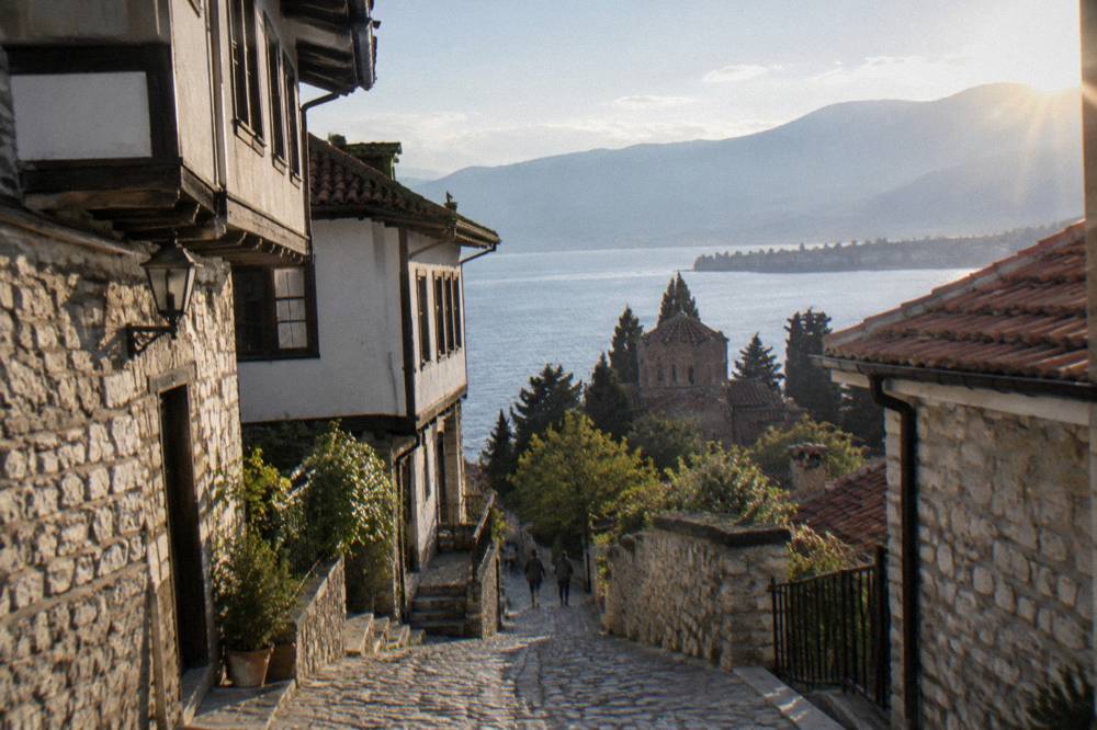 A winding road along a lakeshore with a village and steep hills beyond