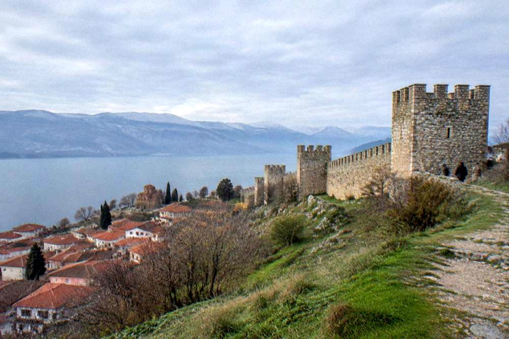 A stone fortress wall on a hill overlooking a lake and distant mountains