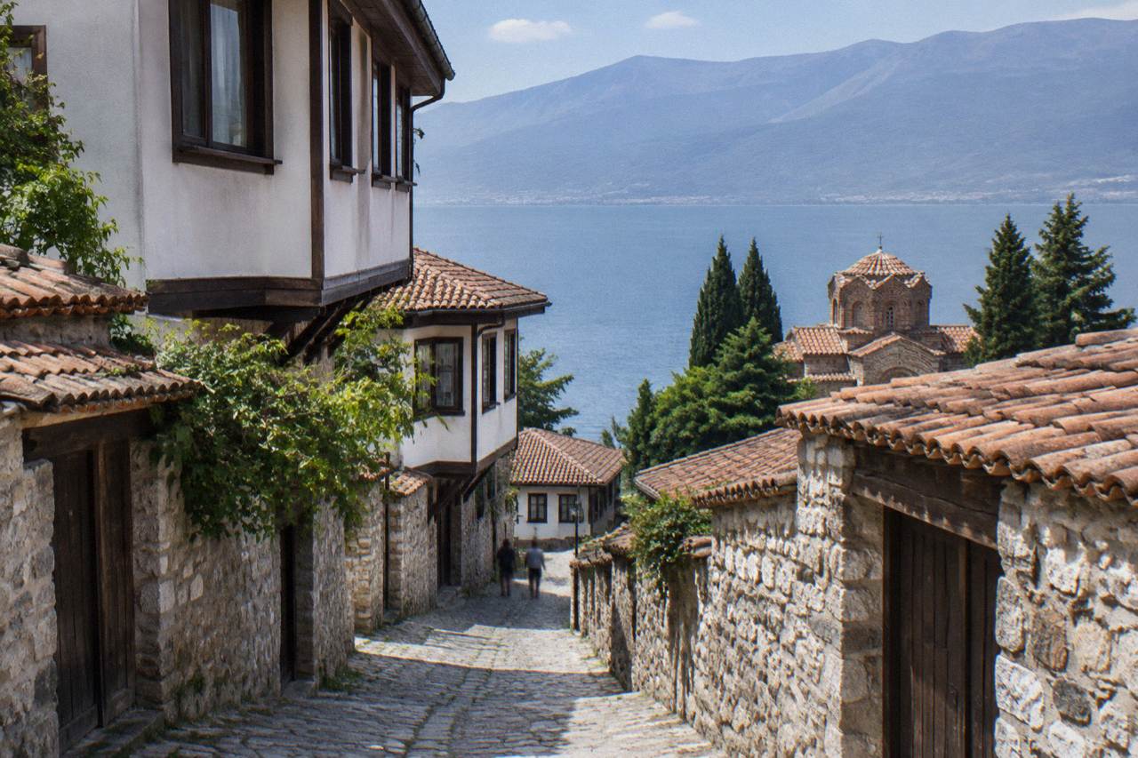 A lakeside town climbing a hillside above a wide blue mountain lake, with church domes and red roofs above the shoreline
