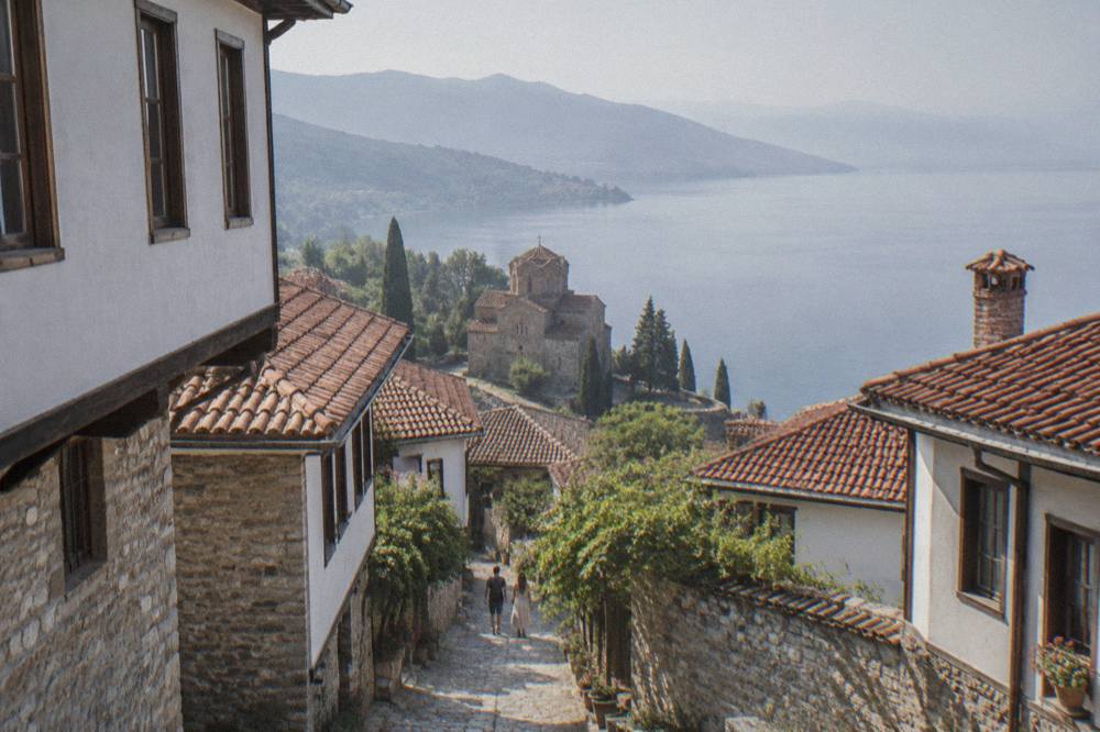 A stone church on a cliff above a calm blue lake, with wooded hills receding along the far shoreline