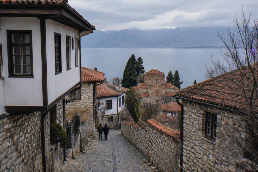 A hillside town with many small church domes and tiled roofs rising above a blue lake