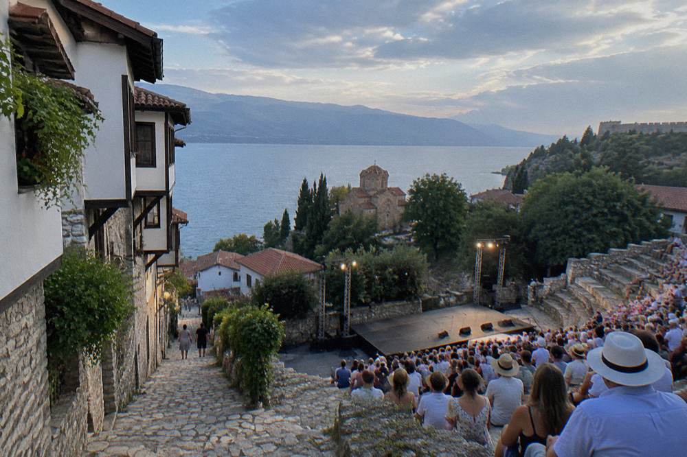 Open-air stone theatre seating filled with an evening audience under lights