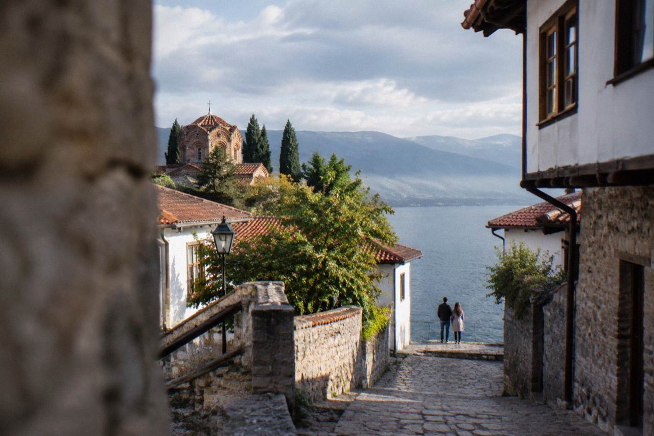A couple standing on the stone quay of Ohrid at dusk with the lake and hills behind them