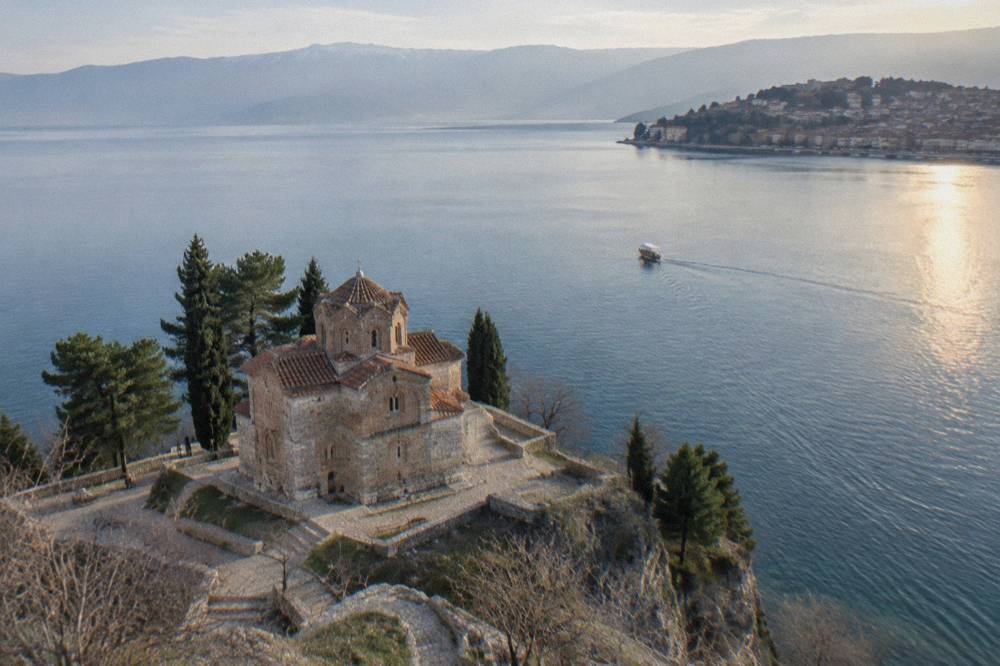 A small boat crossing calm water toward Ohrid old town at sunset