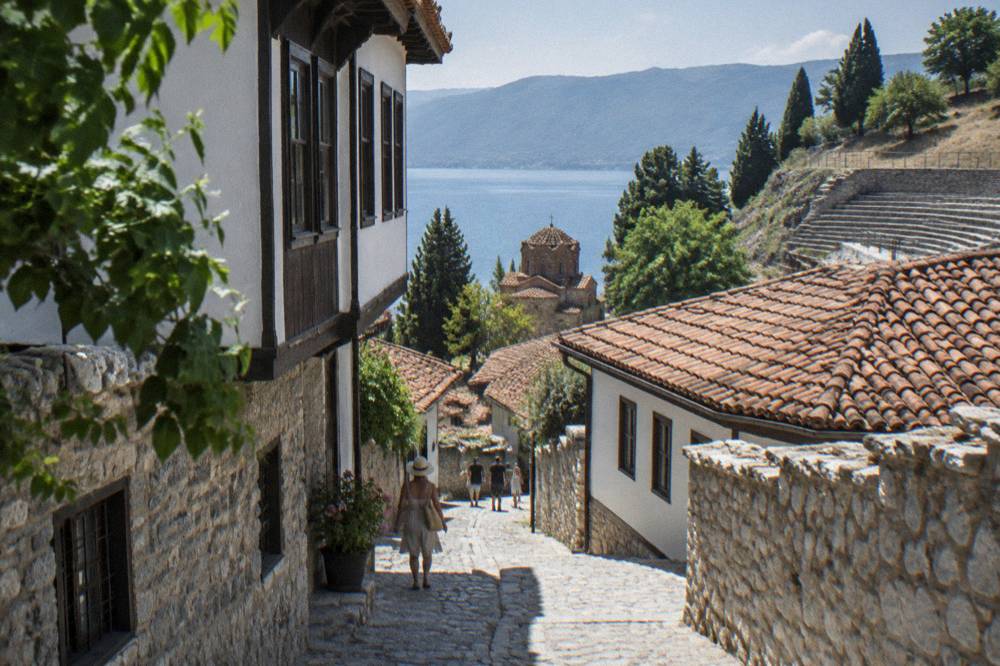 An ancient stone theatre seating area carved into a hillside above red rooftops