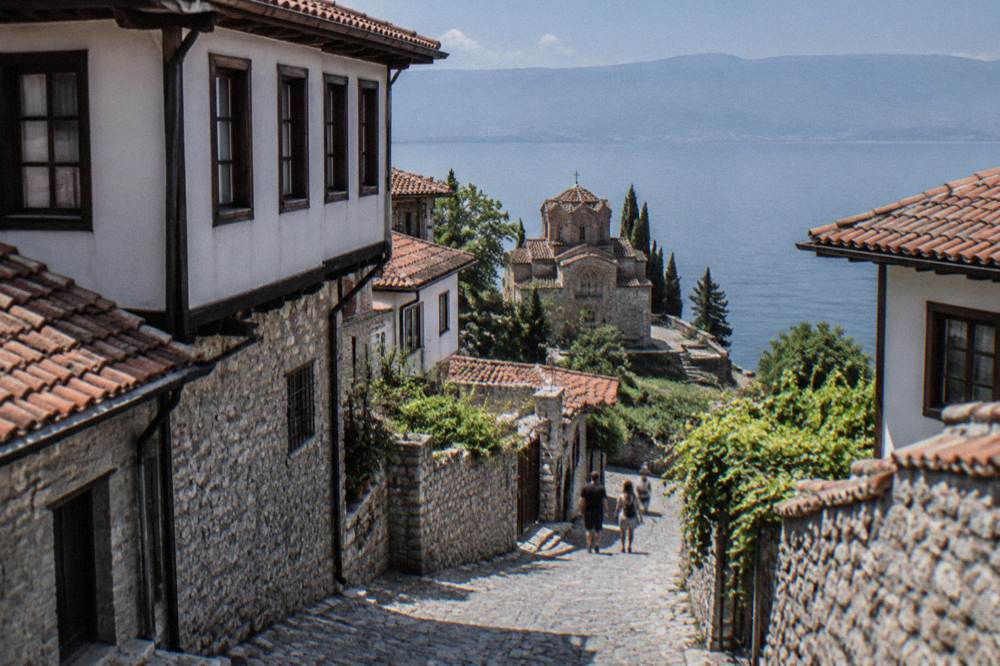 Small stone church on a cliff above a calm blue lake with a terrace below