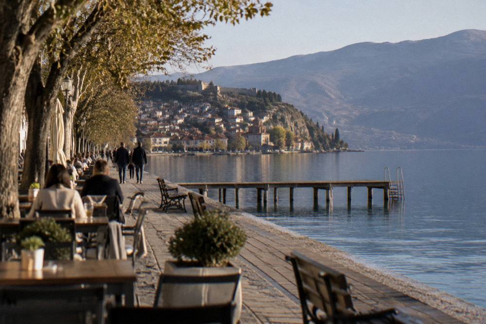 Outdoor restaurant tables beside a lake promenade in late afternoon light