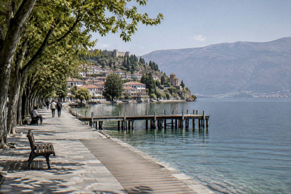 A wooden jetty extending into clear green water near a lakeside village