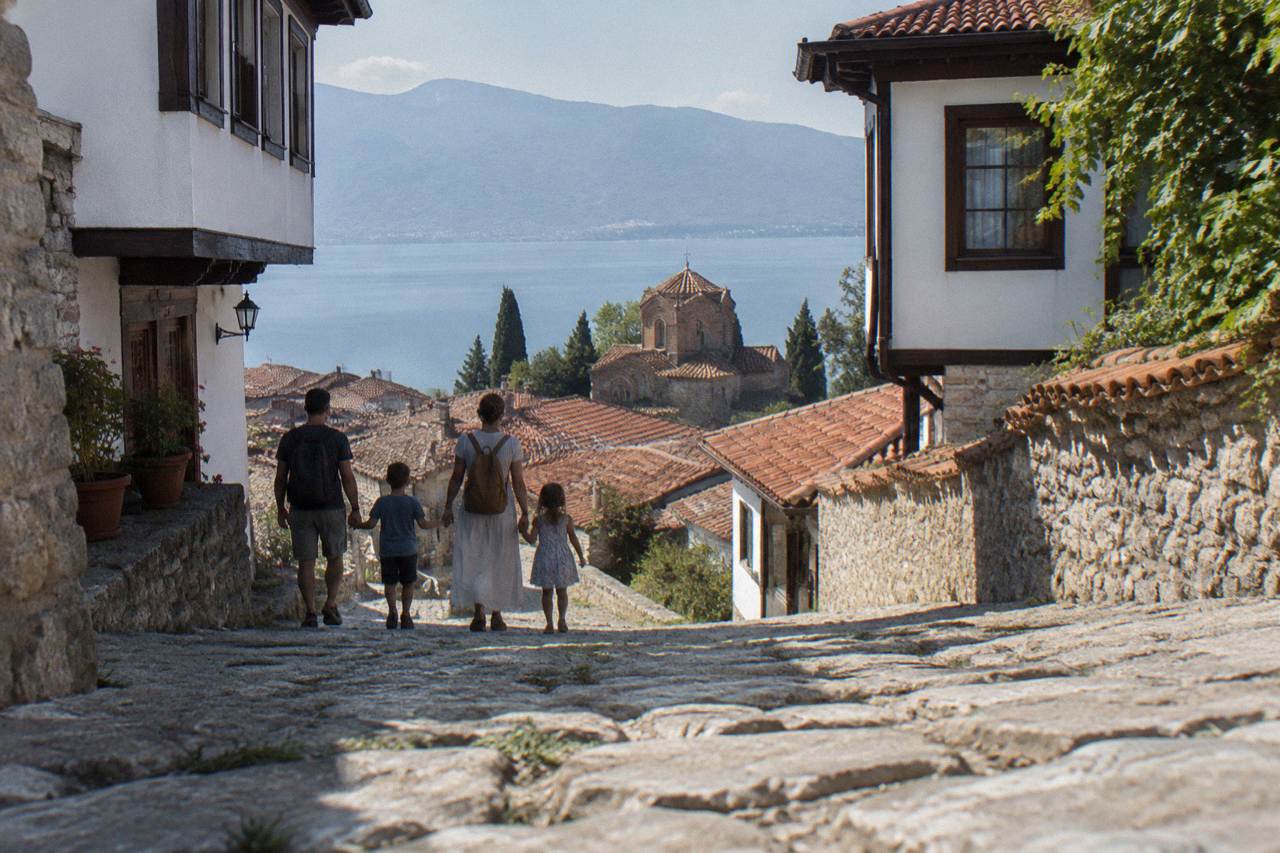 A family walking a cobbled lane above the rooftops of Ohrid old town with Lake Ohrid in the distance