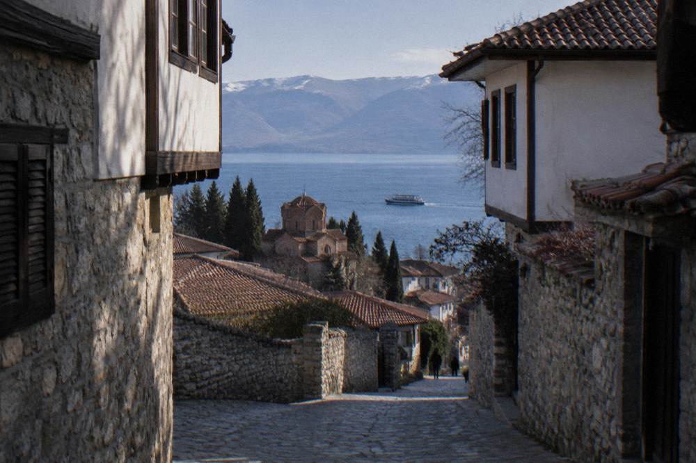 A small tour boat on blue water leaving Ohrid port with the old town behind