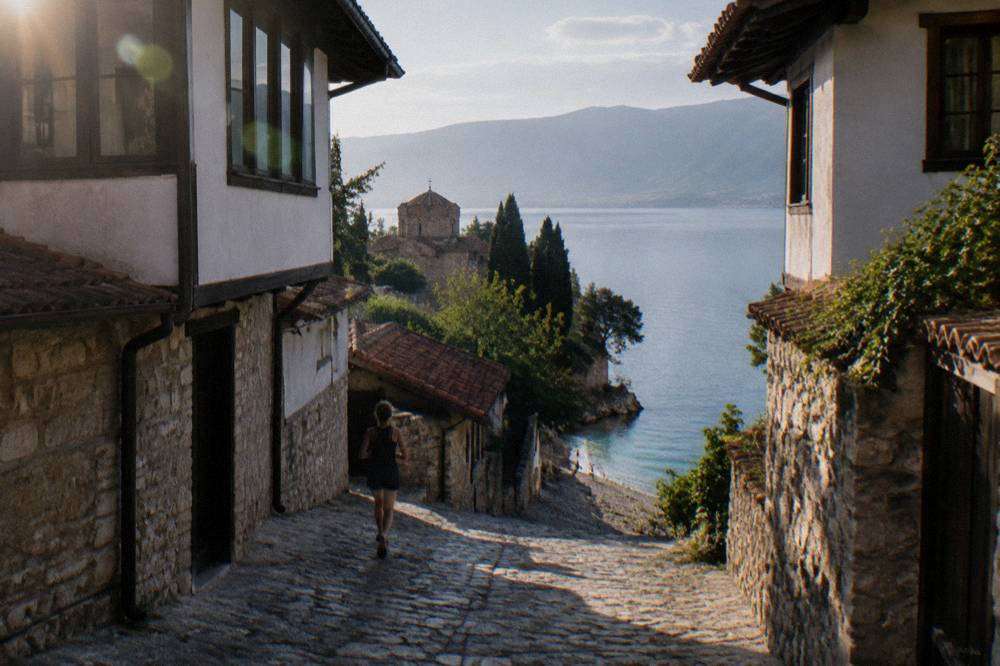 A clear pebble beach on Lake Ohrid with shallow turquoise water and hills beyond