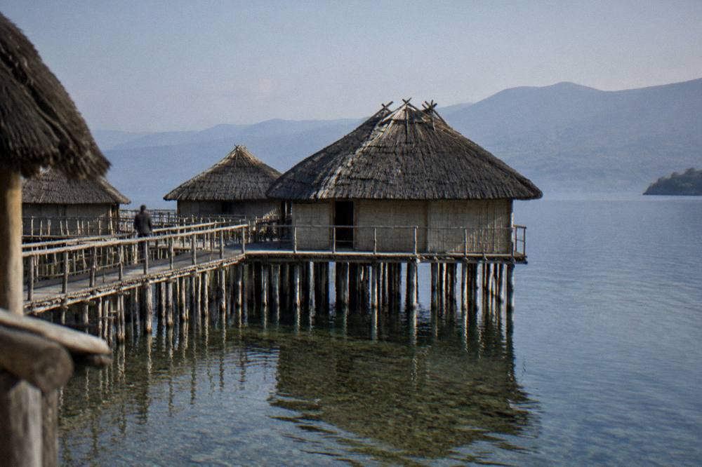 A reconstructed prehistoric pile dwelling standing on wooden posts above the water at the Bay of Bones