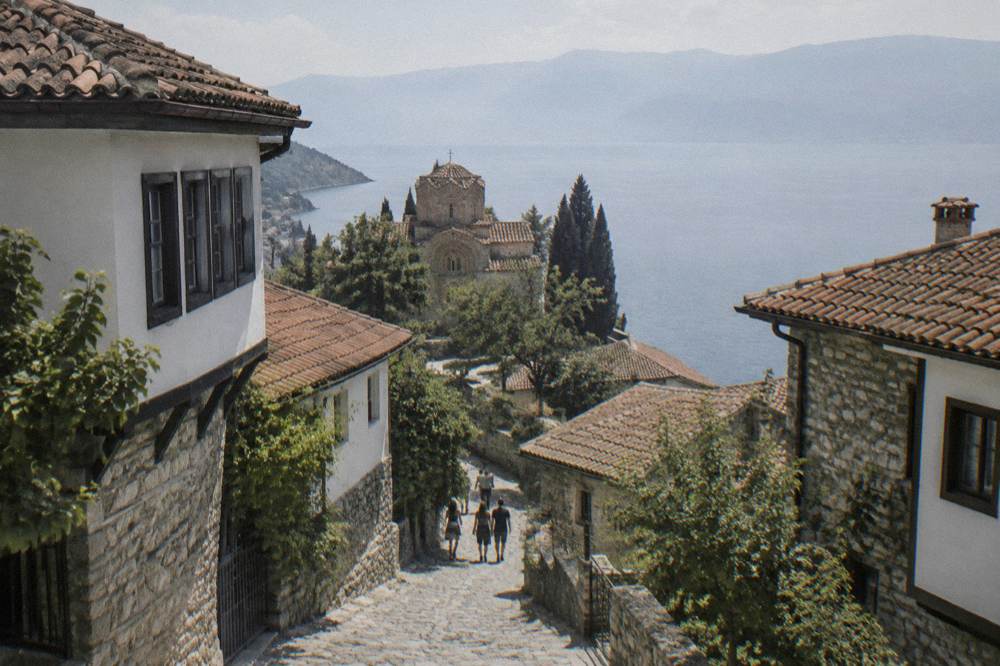 A stone church on a cliff above a calm mountain lake