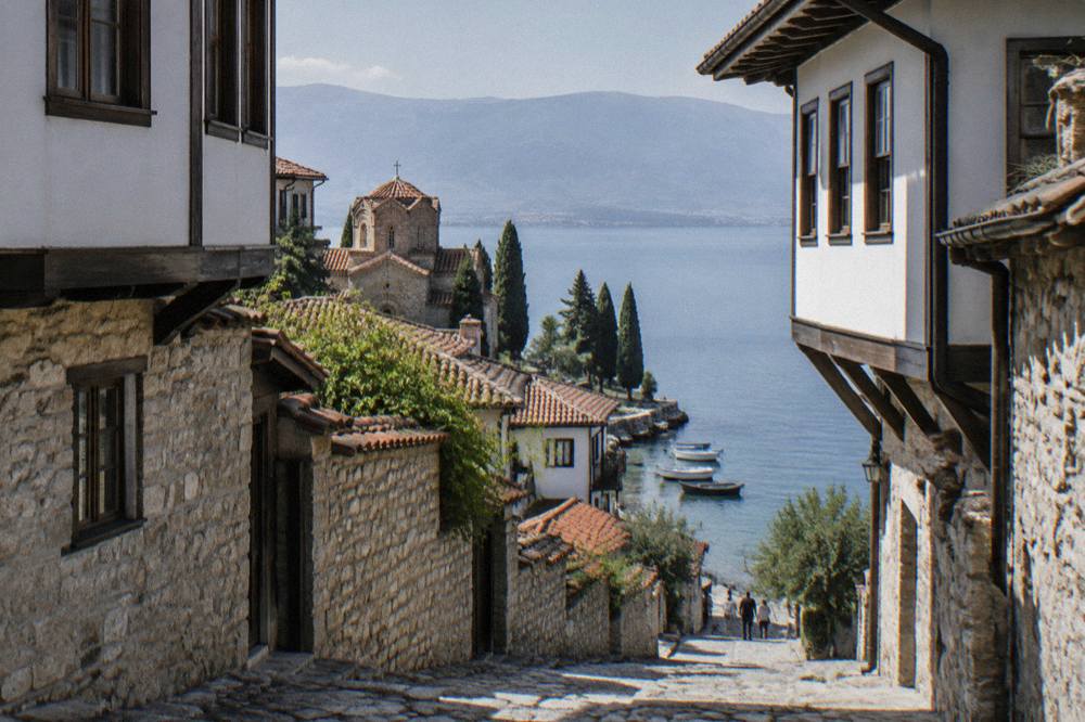 Boats moored on clear green lake water below the old town of Ohrid