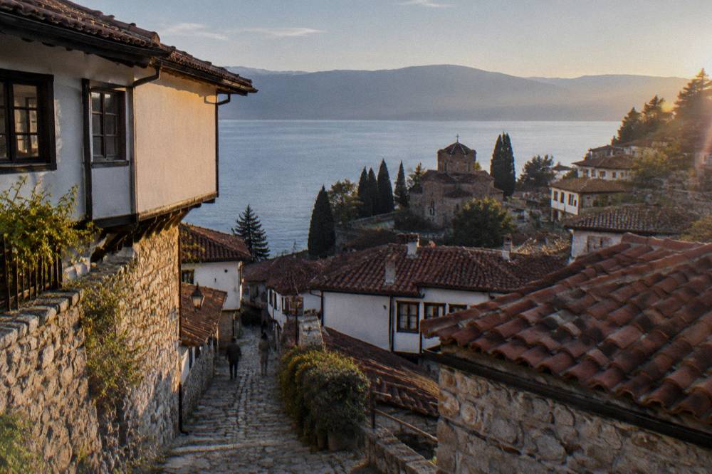 The terraced old town of Ohrid seen from the water at golden hour, with stone houses stacked up a hillside