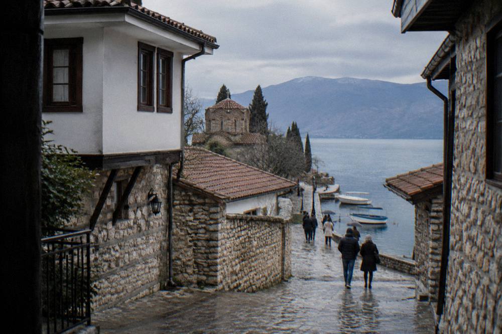 Passengers walking along the stone quay of Ohrid port past moored boats in the morning