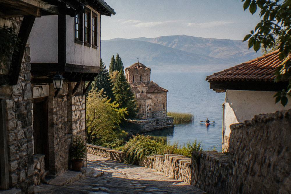 A kayaker paddling past reeds and a stone church foundation at the edge of Lake Ohrid