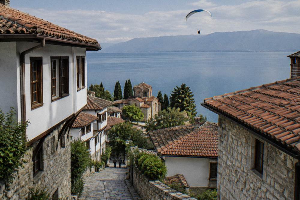 A tandem paraglider flying high above the blue water of Lake Ohrid and the town rooftops