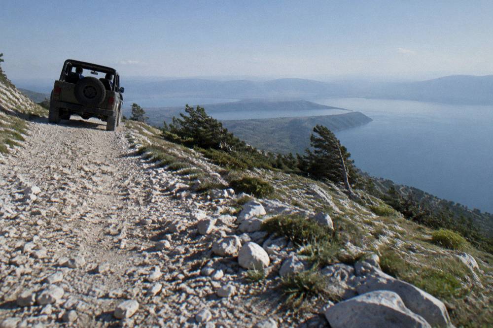 An open jeep on a gravel track high on the Galicica ridge with two blue lakes on the horizon