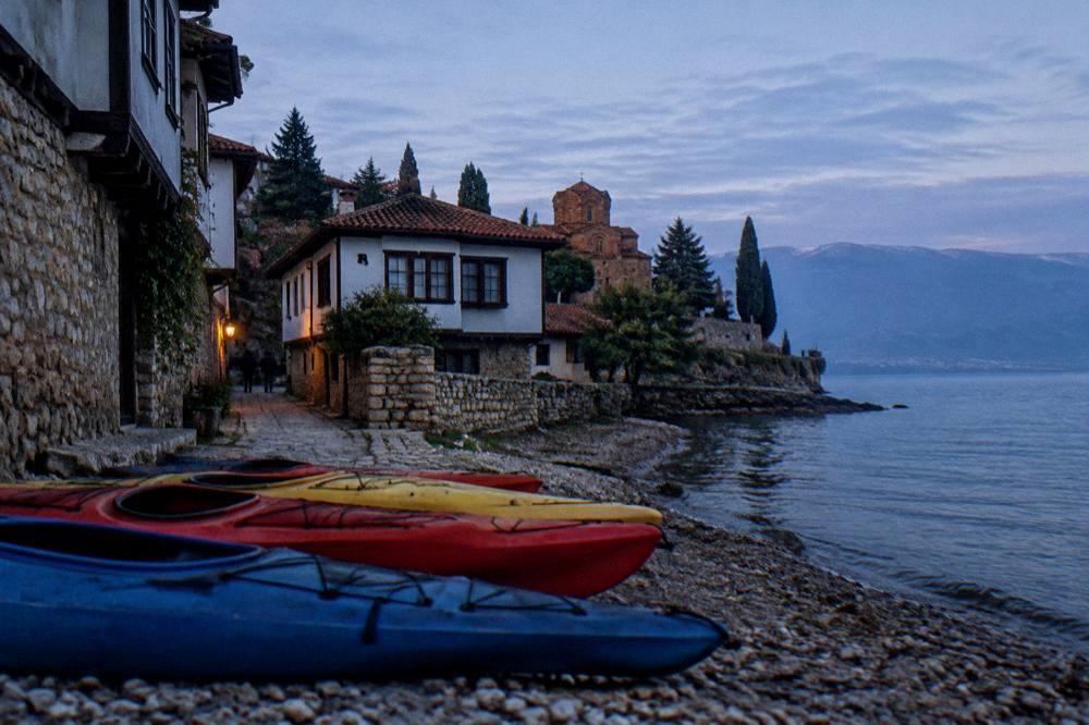 A row of kayaks pulled up on a pebble beach with the old town of Ohrid in the background