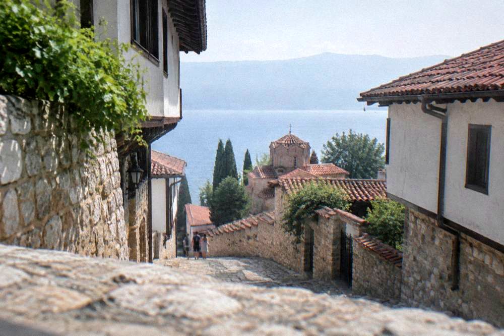 White church walls and red roofs above the blue water of Lake Ohrid seen from a high old town lane