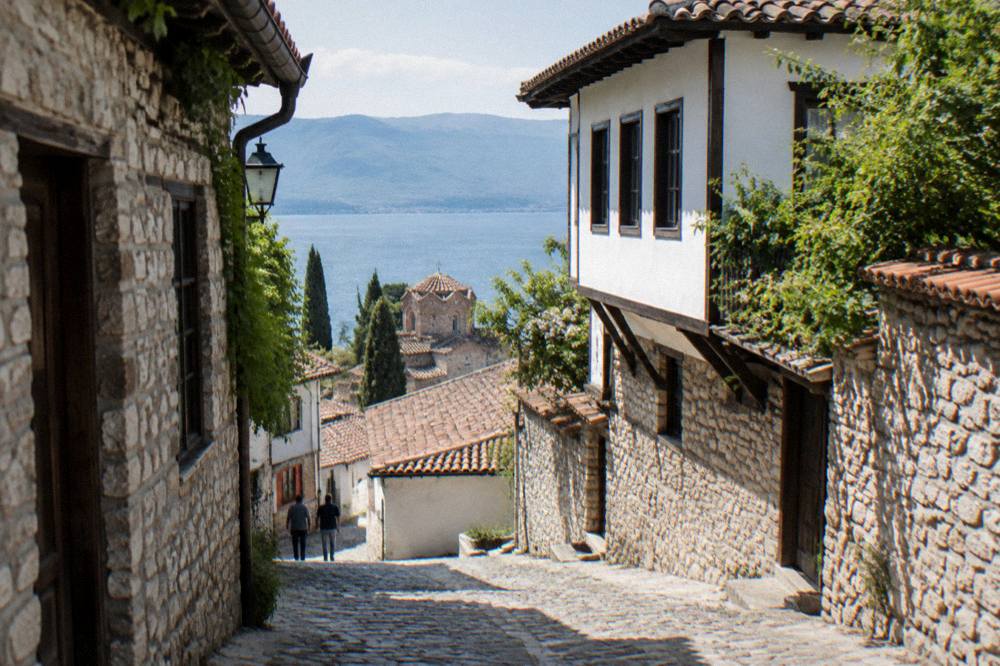 A narrow cobbled Ohrid lane with old stone houses and a glimpse of the lake at the end